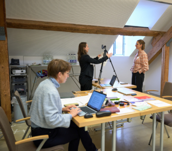 Drei Menschen im Newsroom an der Arbeit. 