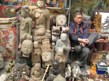 Foto eines asiatischen Mannes, der neben Buddha-Statuen sitzt.